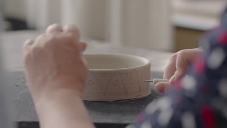 woman hands during painting on ceramic plates. potter workshop of making handcraft clay dishes. artist creates a beautiful pattern on earthenware in a pottery workshop. close-up slow motion