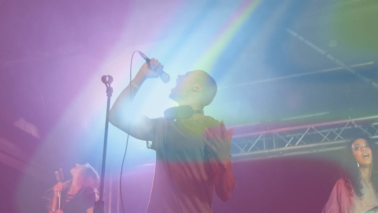Concert vocalist stepping into spotlight belting note to engage crowd as singers shaking tambourine