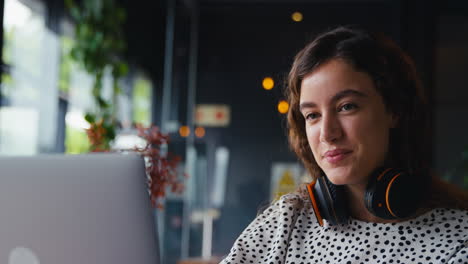 Cerca-De-Una-Mujer-De-Negocios-Usando-Auriculares-Inalámbricos-Trabajando-En-Una-Computadora-Portátil-En-Una-Cafetería-Tomando-Café