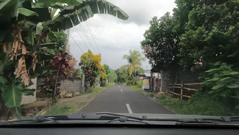 First-person-view-of-driving-a-car-fast-on-countryside-narrow-road-through-balinese-villages-and-lush-tropical-scenery