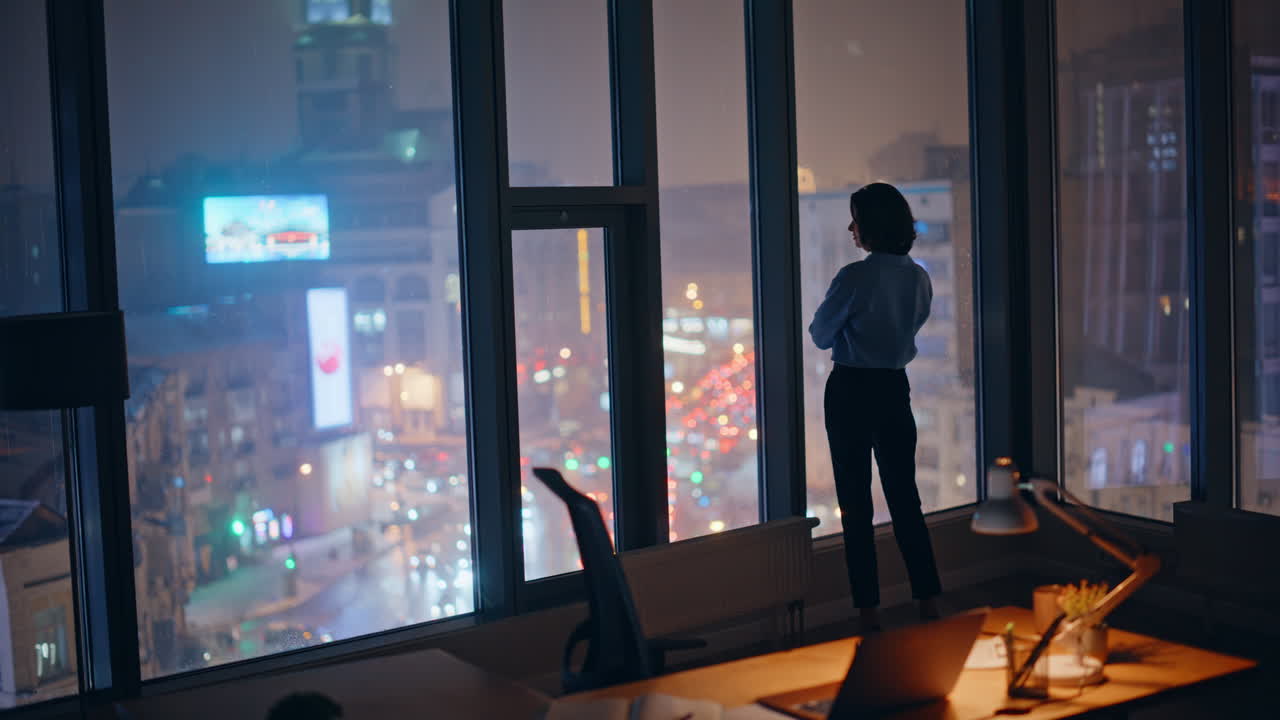 Confident ceo looking night city view from office panoramic window silhouette