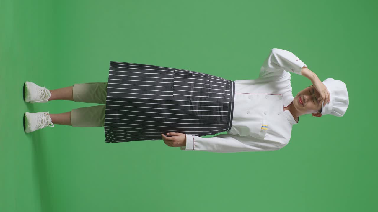 Full Body Of Asian Woman Chef Having A Headache While Standing In The Green Screen Background Studio