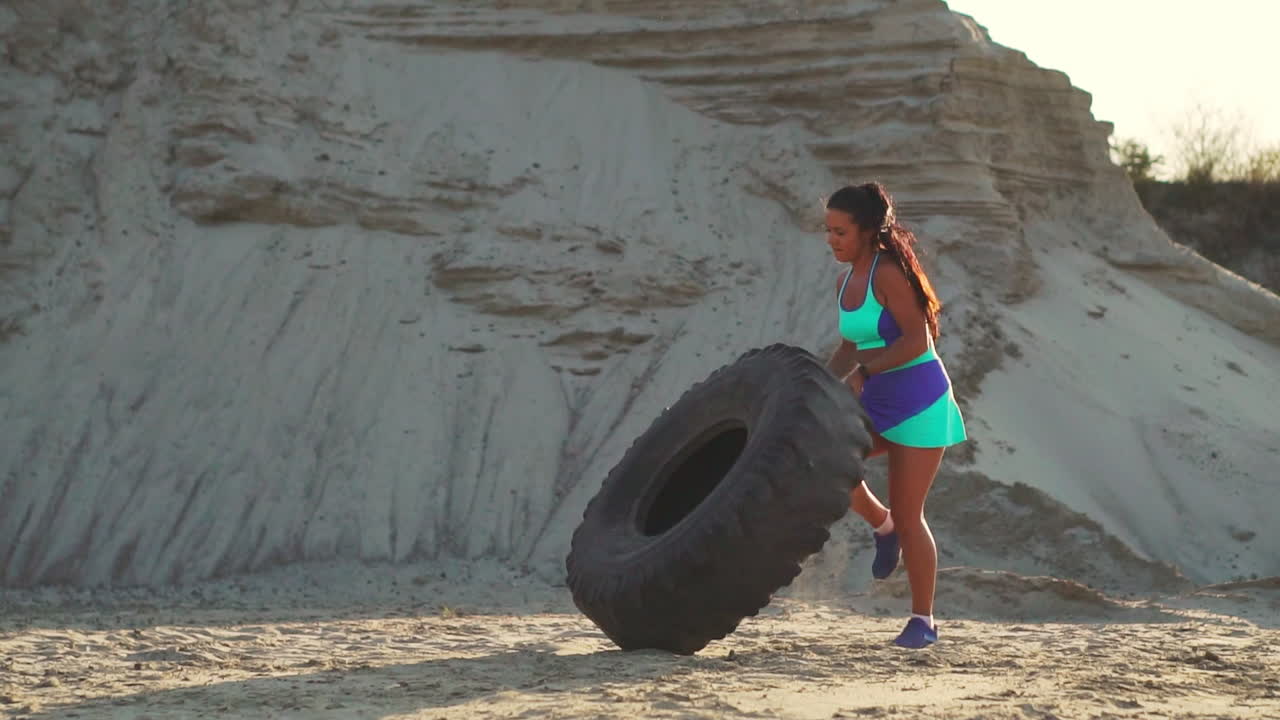 chica en una cantera de arena empujando una rueda en el entrenamiento de crossfit al atardecer en el sol