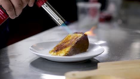 caramelizing superfine sugar on a slice of creme brulee cheesecake with a torch - close up