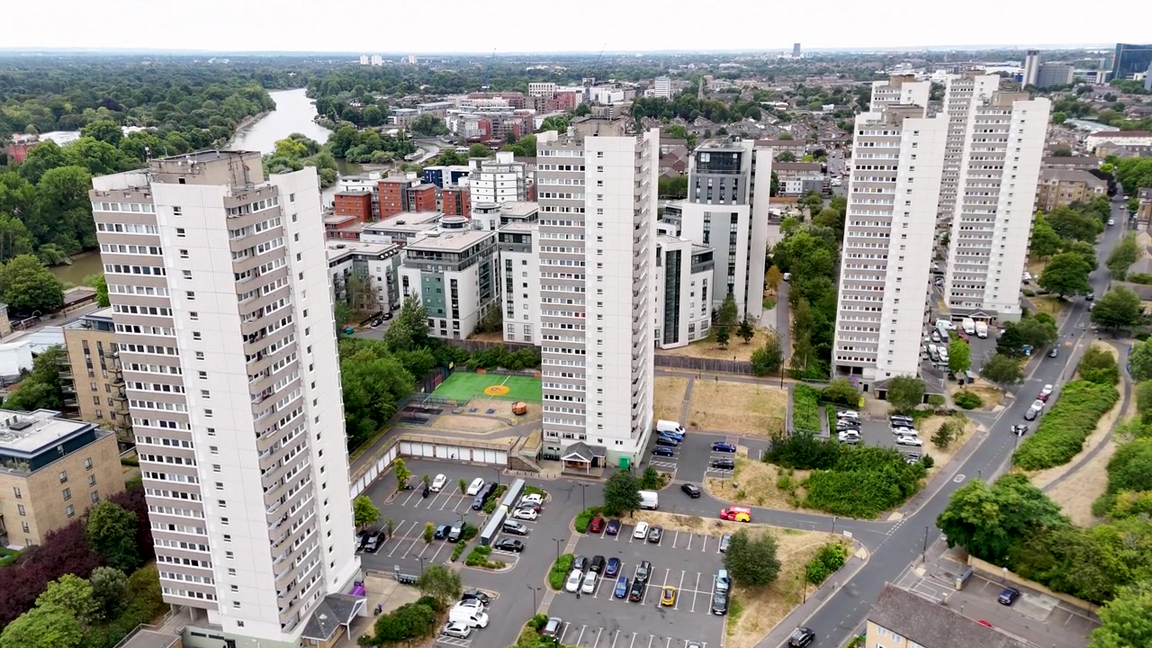 Tre alti condomini a torre comunali del dopoguerra si ergono sopra appartamenti a bassa altezza, parcheggi e alberi maturi in un complesso residenziale