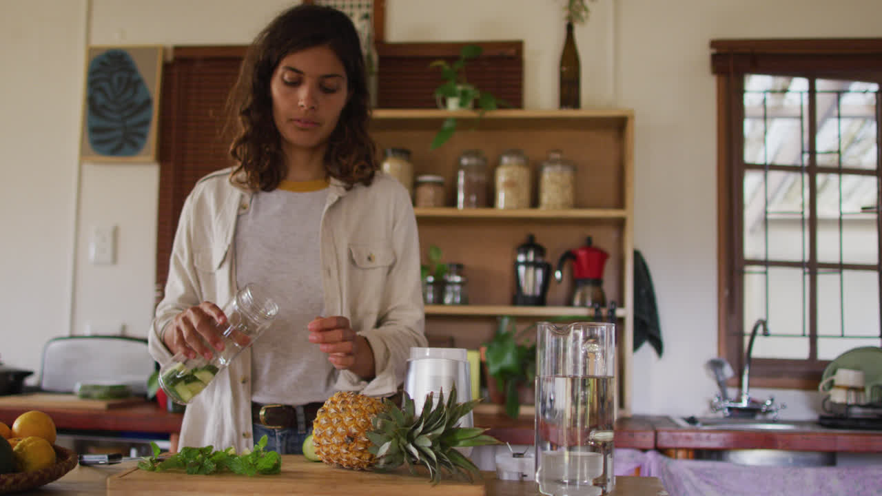 mujer de raza mixta preparando una bebida para la salud de pie en la cocina de la cabaña
