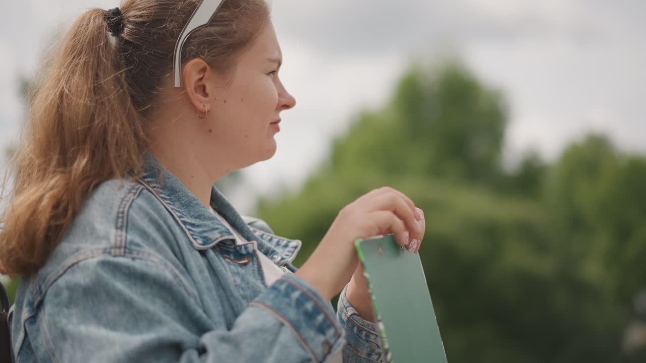 Donna serena che ammira la natura. Donna rilassata vestita in denim che osserva il paesaggio naturale intorno a sé. Donna pacifica che tiene una lavagnetta verde mentre osserva pensierosamente l'ambiente scenografico nel parco.