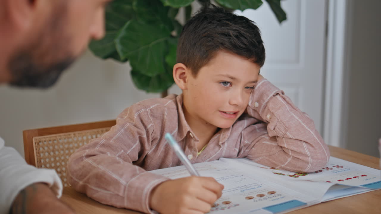 Little schoolboy writing notebook learning distant at home with father closeup