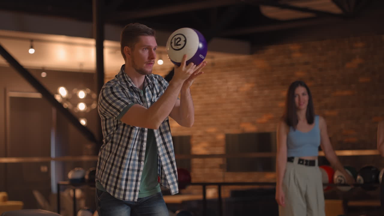 Ritratto: Un giovane uomo effettua il lancio finale con una palla da bowling e vince la partita con il supporto e la gioia dei suoi amici di diverse nazionalità. Esultano e celebrano la vittoria.