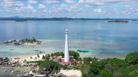 wide aerial of white lighthouse on lengkuas island with belitung on horizon