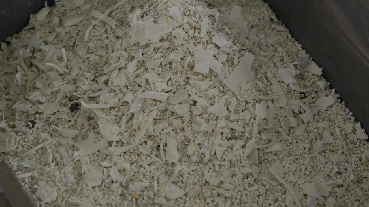 Ovenfra-billede af grove hvide malede plastflager og regranulat inde i en industribeholder.