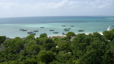 Anchored-boats-on-Zanzibar-coast-with-lush-rainforest,-drone-shot