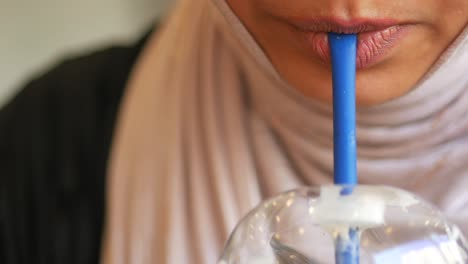 close-up of a person drinking from a plastic cup with a blue straw