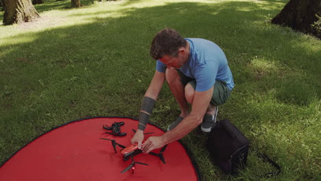 man packs up small drone after flight in park, sunny day, close up