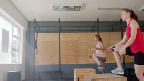 unaltered diverse women jumping on boxes, training at fitness class in gym, slow motion