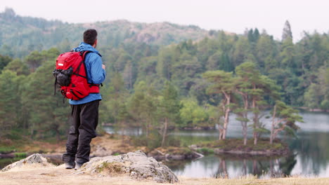 Caucasian-adult-man-on-the-left-shot-standing-on-a-hill-admiring-the-view-of-a-lake,-back-view,-Lake-District,-UK