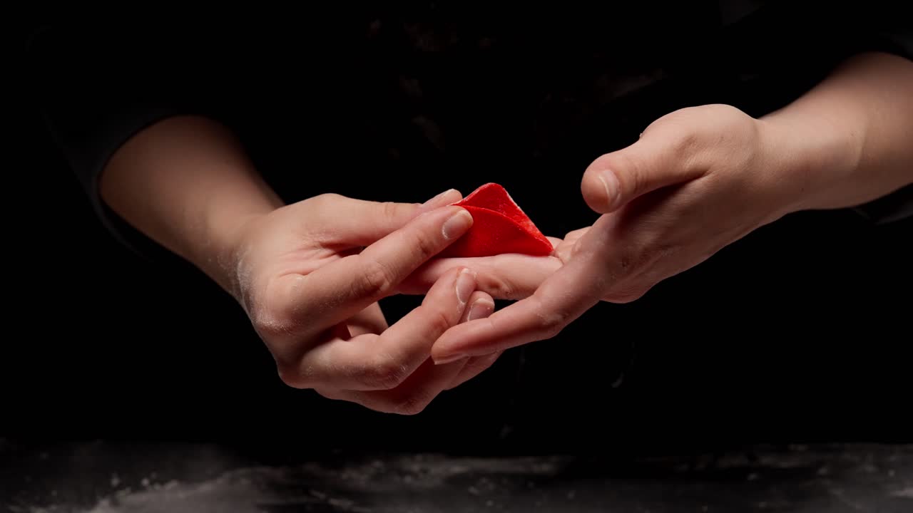 Mani dello chef che piegano la carne in una sfoglia rossa per ravioli