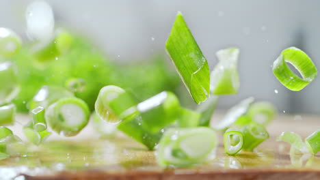 un puñado de cebolla picada cae en un mostrador de la cocina, salpicando gotas de agua en macro y cámara lenta