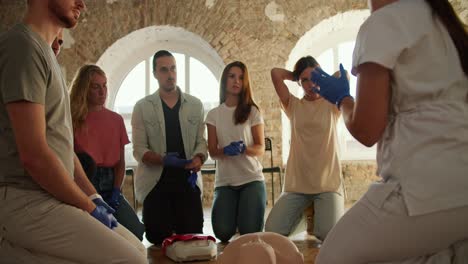 close-up shot: a group of people listening to a professional nurse at a first aid course in front of white brick walls and large windows