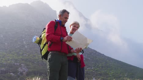 pareja de excursionistas mayores con mochilas leyendo el mapa y apuntando hacia una dirección mientras caminan