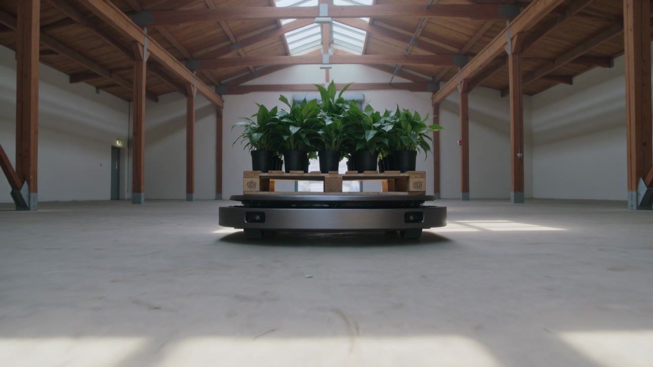 Moving autonomous robot hauling pallet of potted plants through warehouse hall under skylights