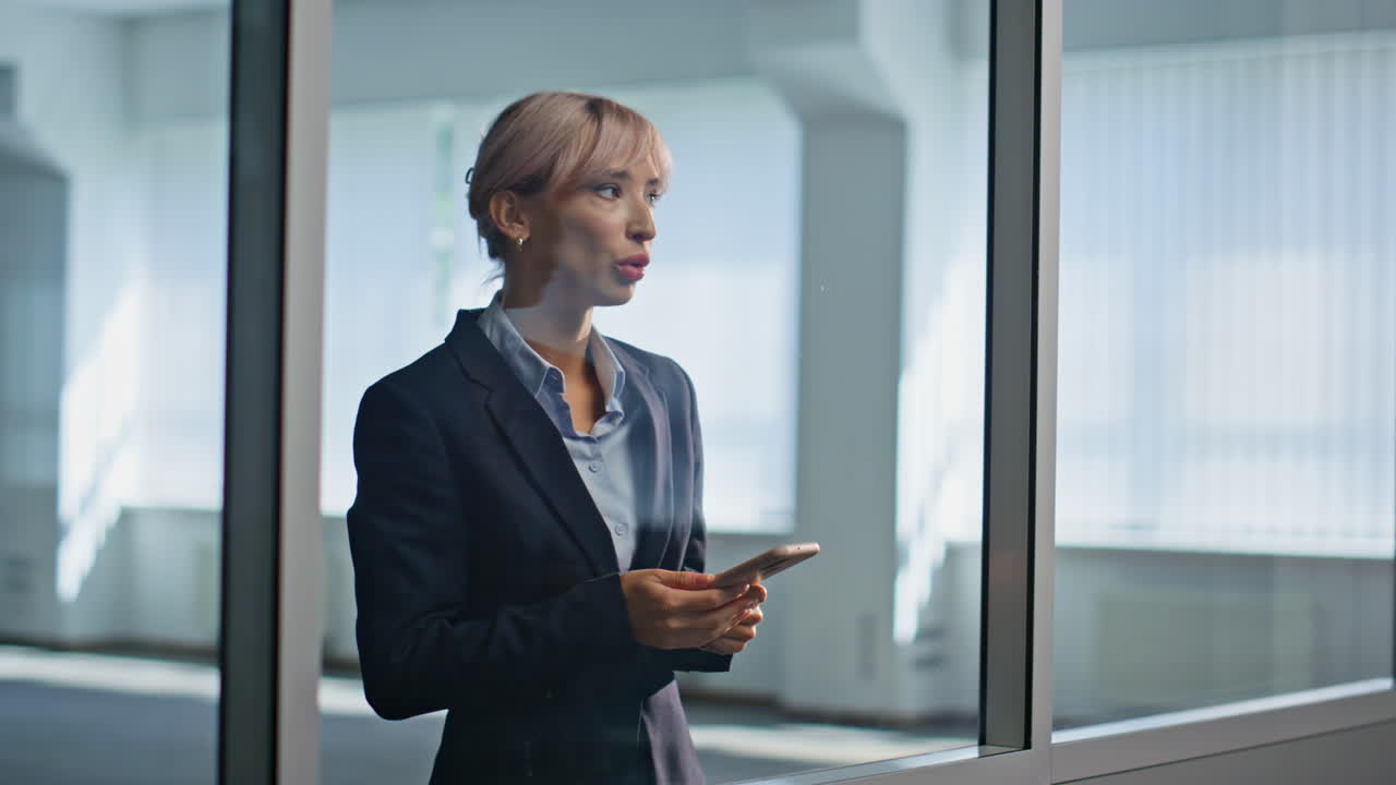Depressed woman swiping cellphone standing alone at glass coworking interior
