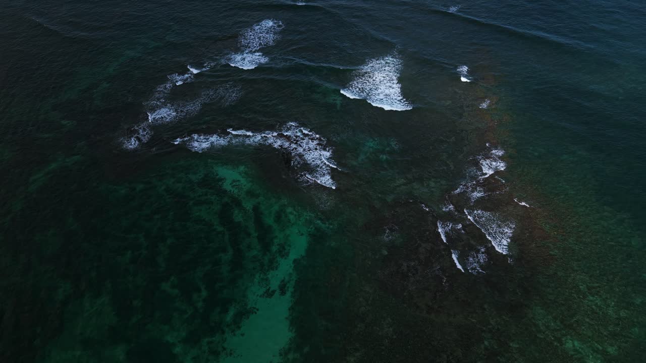 Aerial view of ocean waves breaking on a rocky coast with turquoise and dark water