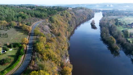 Aerial-view-over-a-river-running-along-a-road-on-cliffs,-Dordogne-River,-France