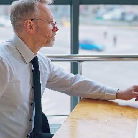 successful businessman on his workplace. senior man in white shirt and a tie works on a laptop. elderly director finishes his work and drinks coffee at the table.