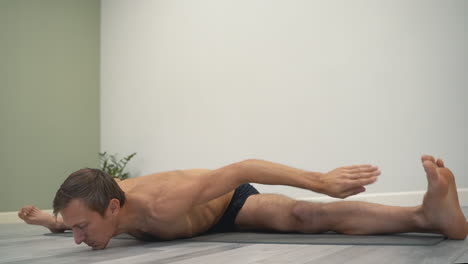 man doing yoga tortoise or turtle pose and upavistha konasana. male athlete doing stretching exercises indoors.