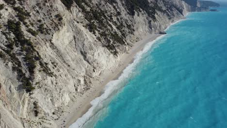 Tilt-down-shot-on-the-blue-waves-of-the-Aegean-sea-hitting-the-shore-of-the-Egremni-beach-in-Lefkada,-Greece