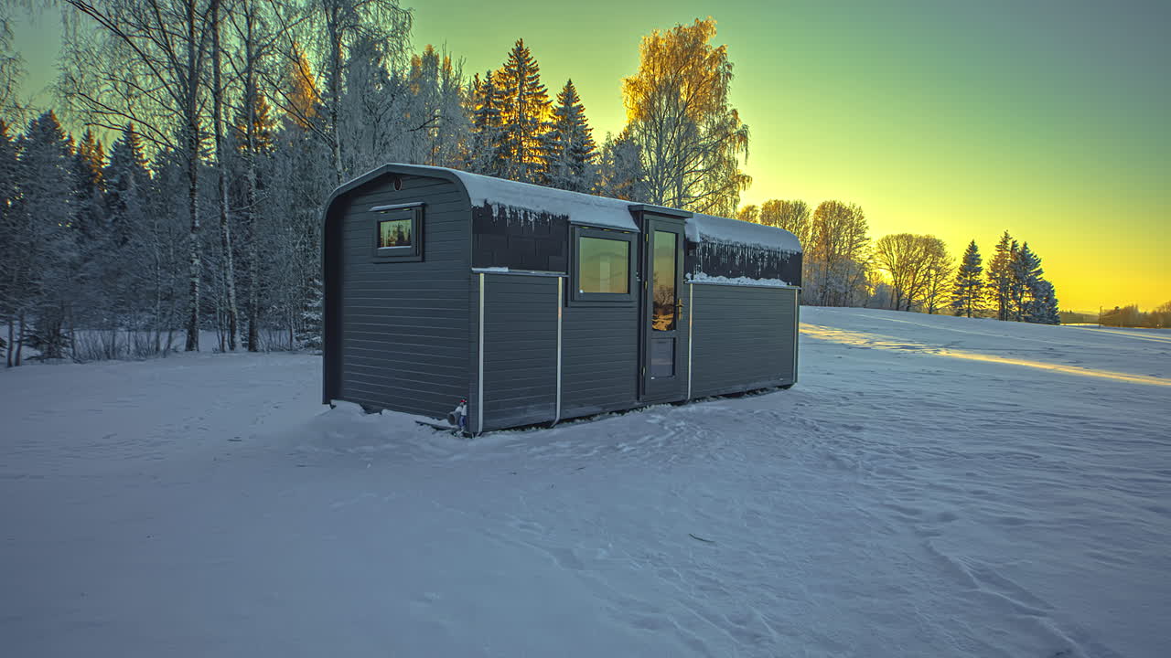 lapso de tiempo de la cabaña de madera para las vacaciones de invierno en el campo nevado con árboles cubiertos de nieve - hermoso cielo amarillo después del atardecer