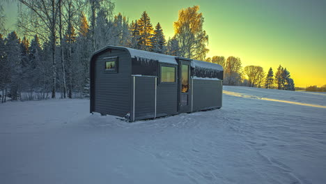 Zeitraffer-Des-Holzhüttenhauses-Für-Winterferien-Auf-Schneebedecktem-Feld-Mit-Schneebedeckten-Bäumen---Schöner-Gelber-Himmel-Nach-Sonnenuntergang