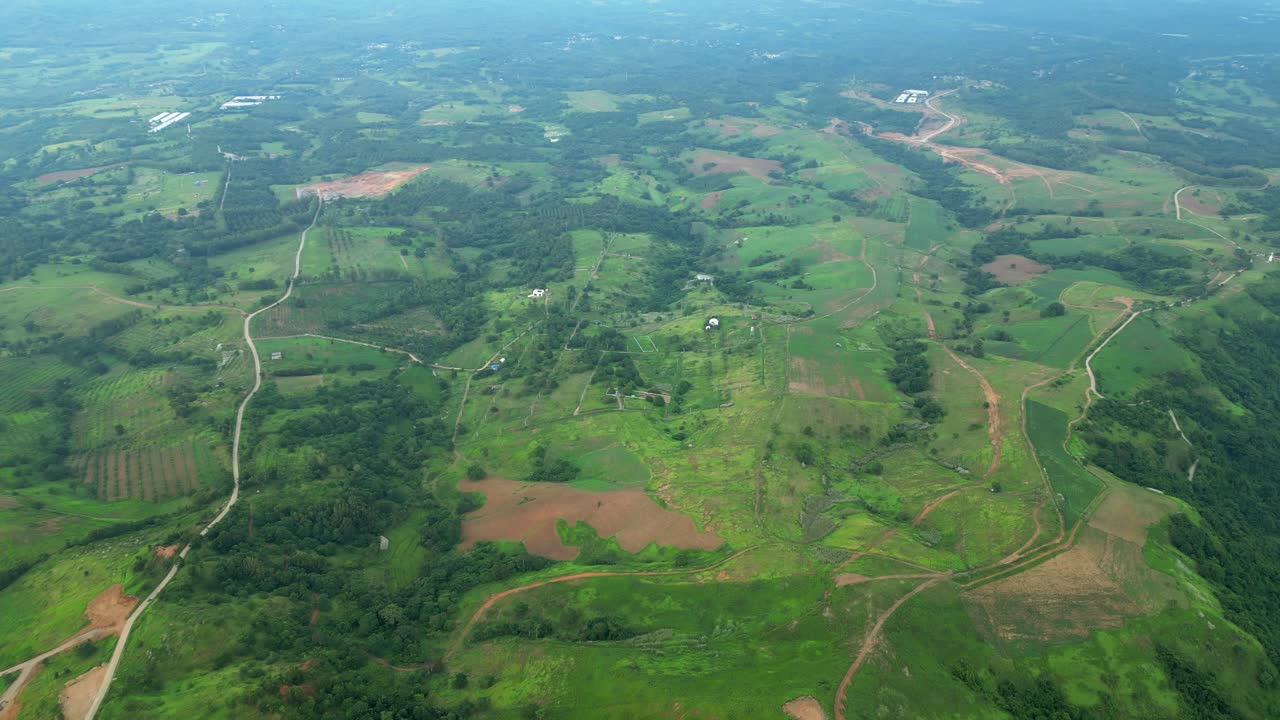 A slow right pan high aerial revealing rolling hills, winding dirt roads, scattered fields, and forest patches, across the rural terrain in Quinawan mountain view, Mariveles Bataan, Philippines