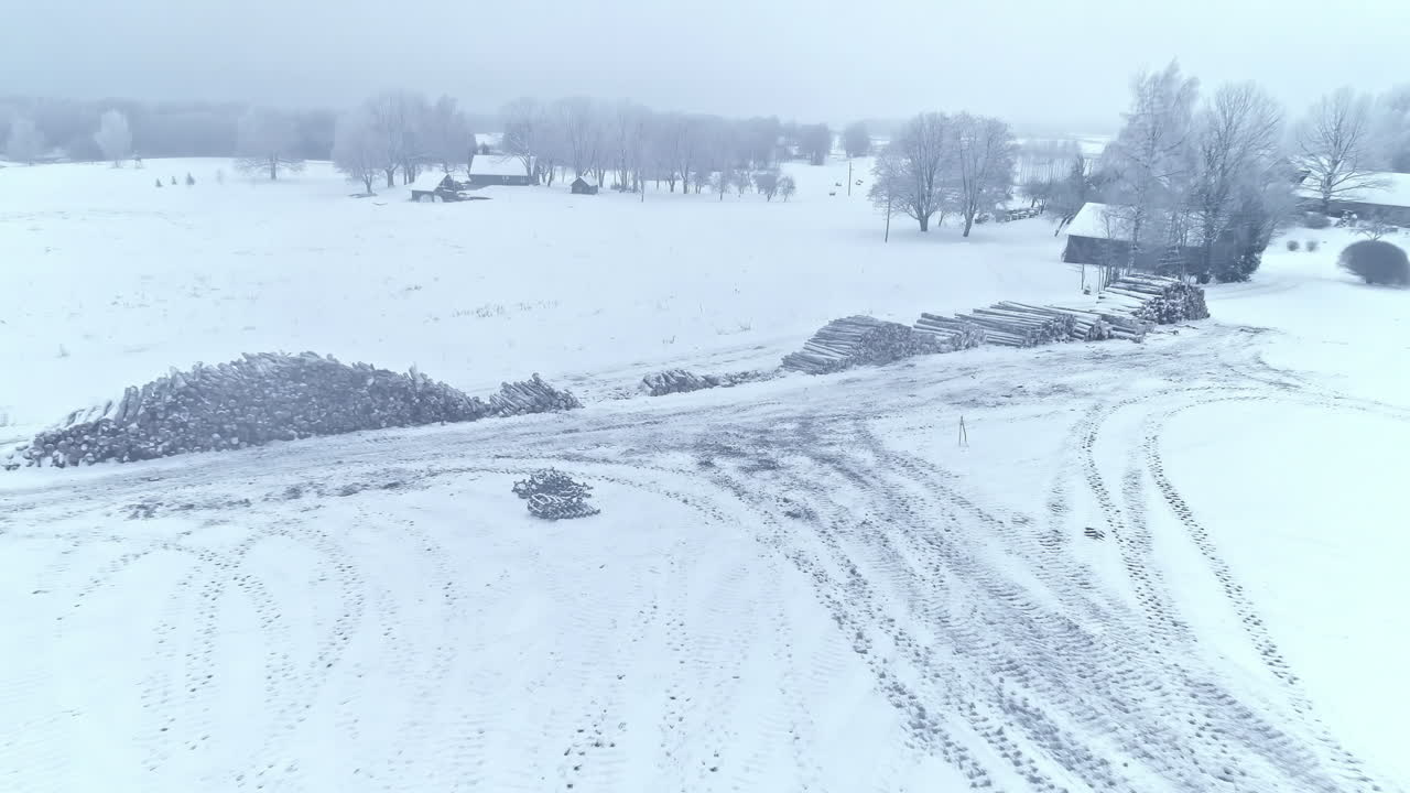 숲이 황폐화되는 동안 쌓인 잘린 나무가 있는 눈 덮인 겨울 들판의 공중 하강 샷