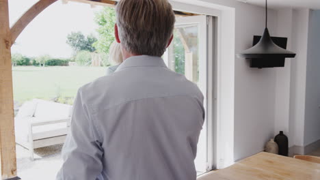 senior couple walk out of kitchen and through patio doors to look at garden