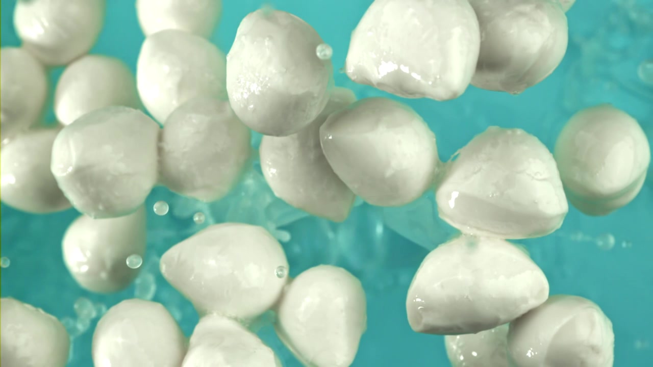Palline di mozzarella fresca che schizzano nell'acqua su sfondo blu.