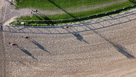 vertical straight down view at trainers on horseback with horses galloping on the racecourse at hipodromo argentino de palermo, buenos aires, static shot