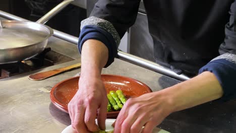 Chef-is-food-plating-a-salad-composed-by-asparagus,-zucchini,-spinach,-roasted-peppers-and-mushrooms,-in-an-clay-plate-over-the-kitchen-counter-in-a-Spanish-restaurant