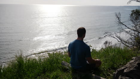 a fit young man in silhouette sitting and practicing meditation and mindfulness in a lotus pose in nature on an ocean cliff at the beach in santa barbara, california