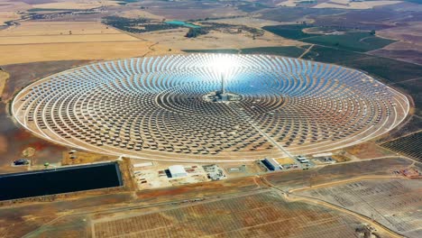 large circular power plant of solar panels in spain. there is the reflection of the sun in the the panels which produce renewable energy, solar energy - aerial view with a drone - environment concept