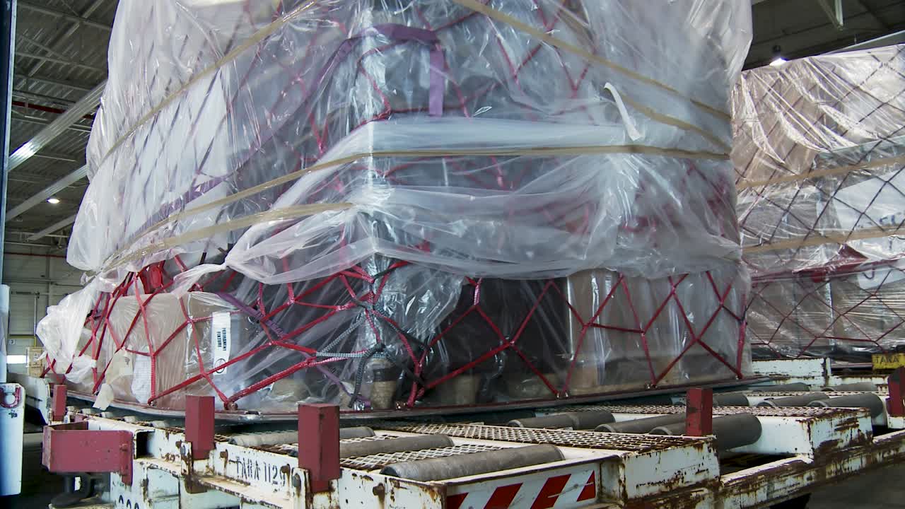 Large cargo wrapped in plastic and netting sits in industrial warehouse