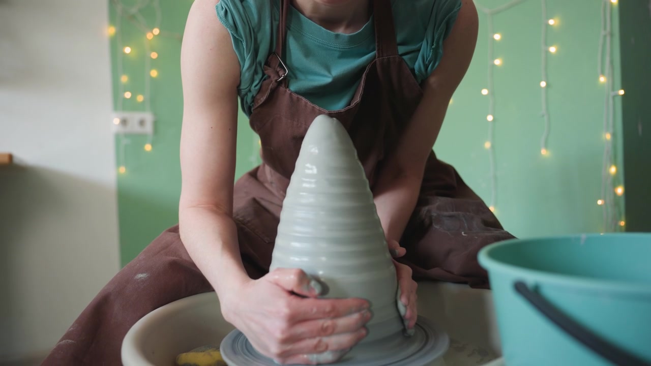 Keramikkünstlerin bei der Arbeit. Eine Frau töpfert an der Töpferscheibe. Ruhiges Atelier mit einer engagierten Frau, die gewissenhaft Ton modelliert. Eine konzentrierte Töpferin formt geschickt und lautlos feuchten Ton an der Töpferscheibe.