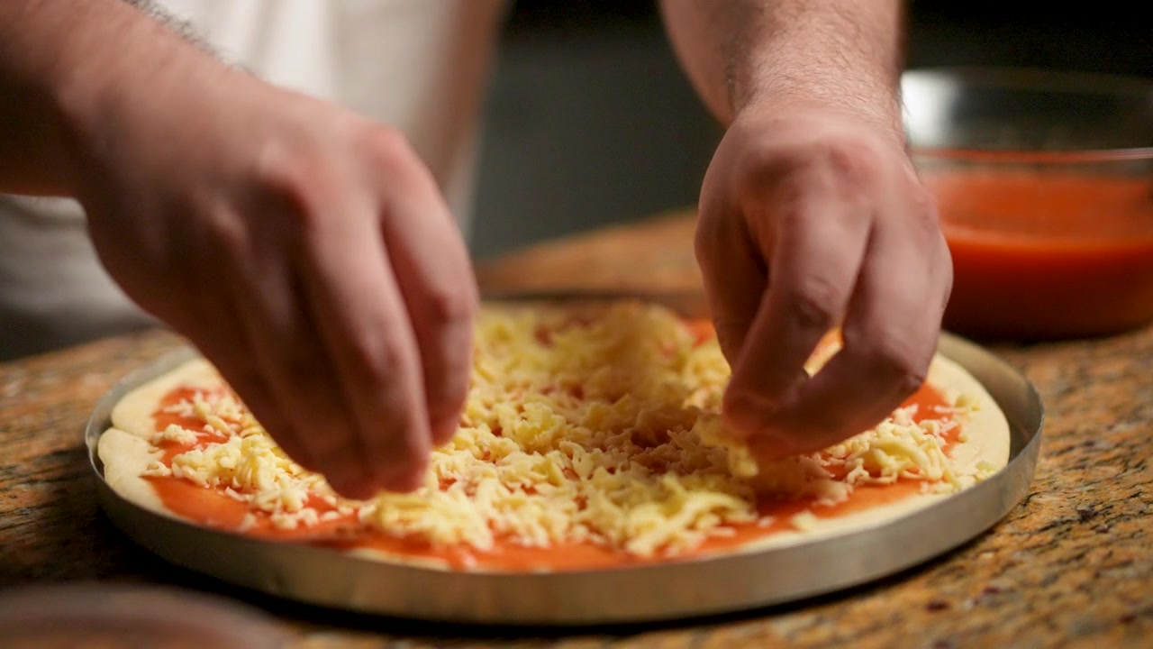 Il processo passo-passo di uno chef per la preparazione di una pizza fatta a mano, dall'applicazione della salsa di pomodoro fresca all'aggiunta di una spolverata di formaggio grattugiato.