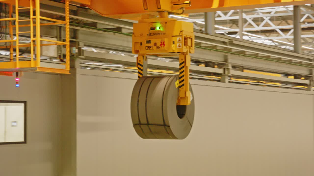 Close up of a overhead bridge crane moving a heavy steel coil in an automated warehouse