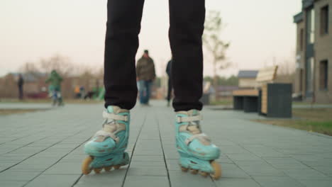 una mujer está patinando a lo largo de un camino pavimentado en un parque, con una chaqueta de melocotón y pantalones negros. el fondo revela una escena animada con otros visitantes del parque, incluido un niño en una bicicleta y personas