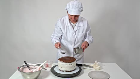 una panadera de mediana edad vierte jarabe en un pastel de boda con brownies de chocolate.