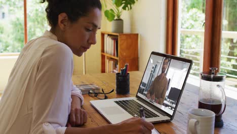 Mixed-race-businesswoman-sitting-at-desk-using-laptop-having-video-call-with-male-colleague