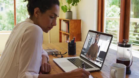 mixed race businesswoman sitting at desk using laptop having video call with male colleague