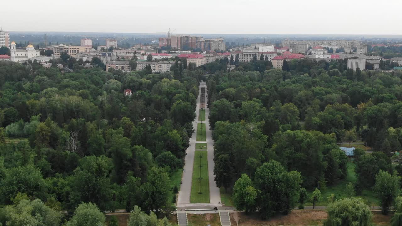 vista aérea de la acera que atraviesa el parque rodeado de árboles que conducen a la ciudad en el fondo